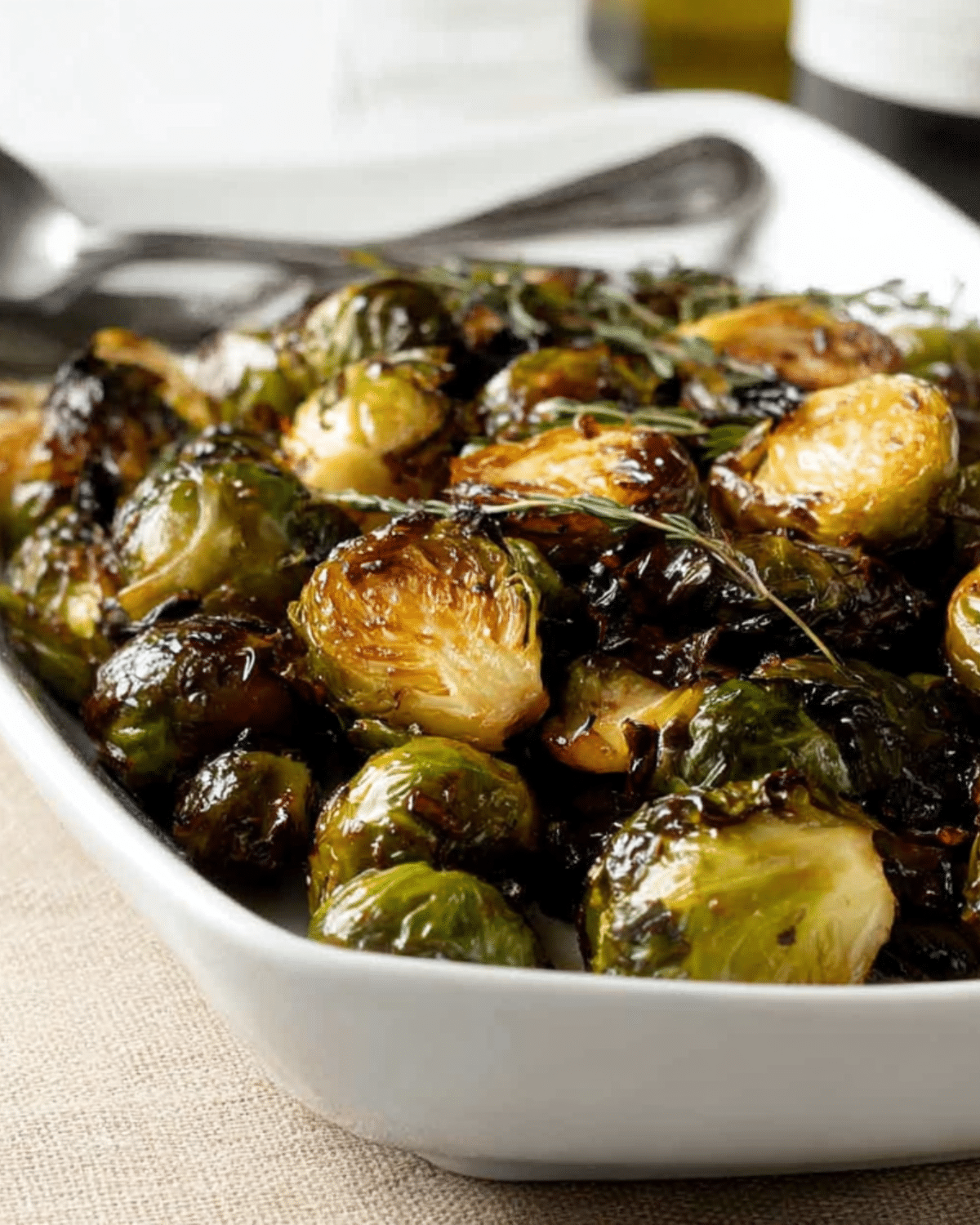 Roasted Balsamic Glazed Brussels Sprouts served in a white dish with fresh herbs.