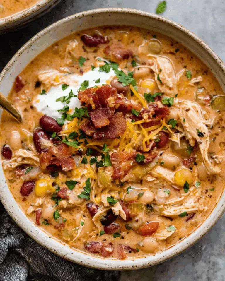 Bowl of creamy crack chicken chili topped with shredded cheese, bacon bits, sour cream, and fresh herbs.