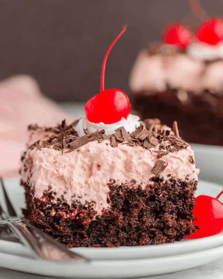 Slice of Cherry Dr Pepper Cake topped with cherry whipped frosting, chocolate shavings, and a maraschino cherry.