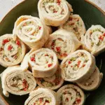 A plate of colorful Christmas Pinwheels made with tortilla wraps, cream cheese, and diced vegetables.