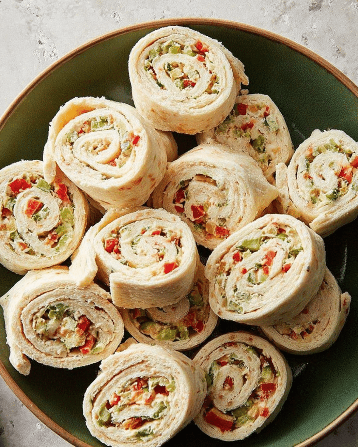 A plate of colorful Christmas Pinwheels made with tortilla wraps, cream cheese, and diced vegetables.