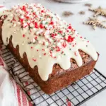 Classic gingerbread loaf topped with white icing and festive red, green, and white sprinkles on a cooling rack.