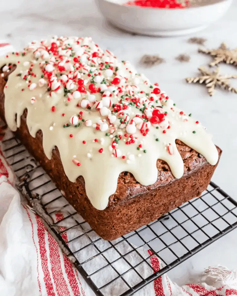 Classic gingerbread loaf topped with white icing and festive red, green, and white sprinkles on a cooling rack.