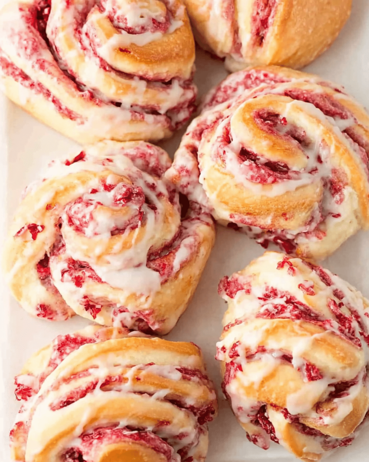 Cranberry Orange Sweet Rolls drizzled with icing on a white platter