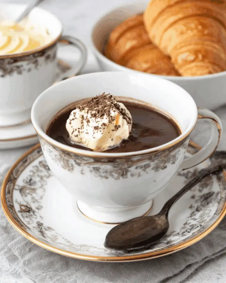 A vintage teacup filled with creamy French hot chocolate topped with whipped cream and chocolate shavings.