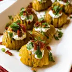 Crispy Loaded Hasselback Potato Bites topped with sour cream, bacon, and herbs on a white platter