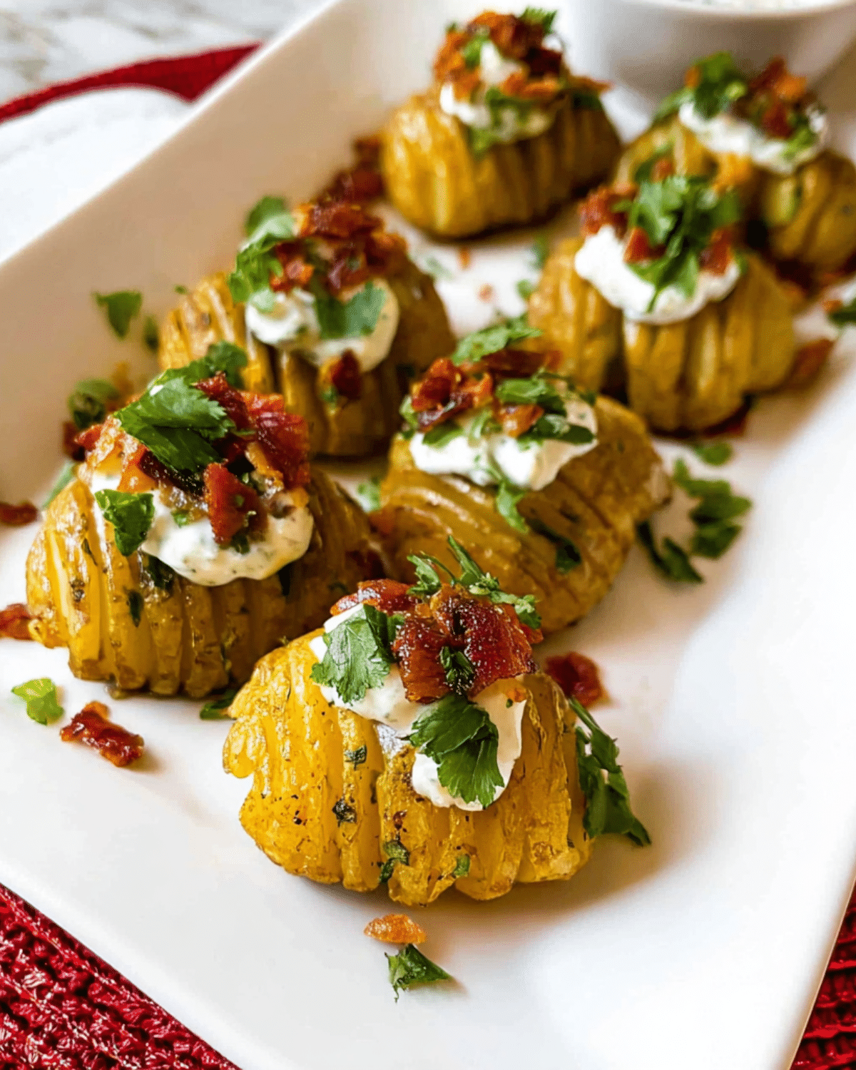 Crispy Loaded Hasselback Potato Bites topped with sour cream, bacon, and herbs on a white platter