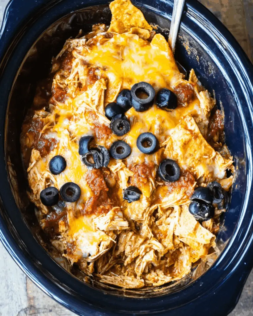 Crockpot chicken enchilada casserole with shredded chicken, melted cheese, salsa, tortilla chips, and sliced black olives.