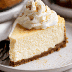 Slice of eggnog cheesecake with a graham cracker crust, topped with whipped cream and sprinkled with nutmeg.