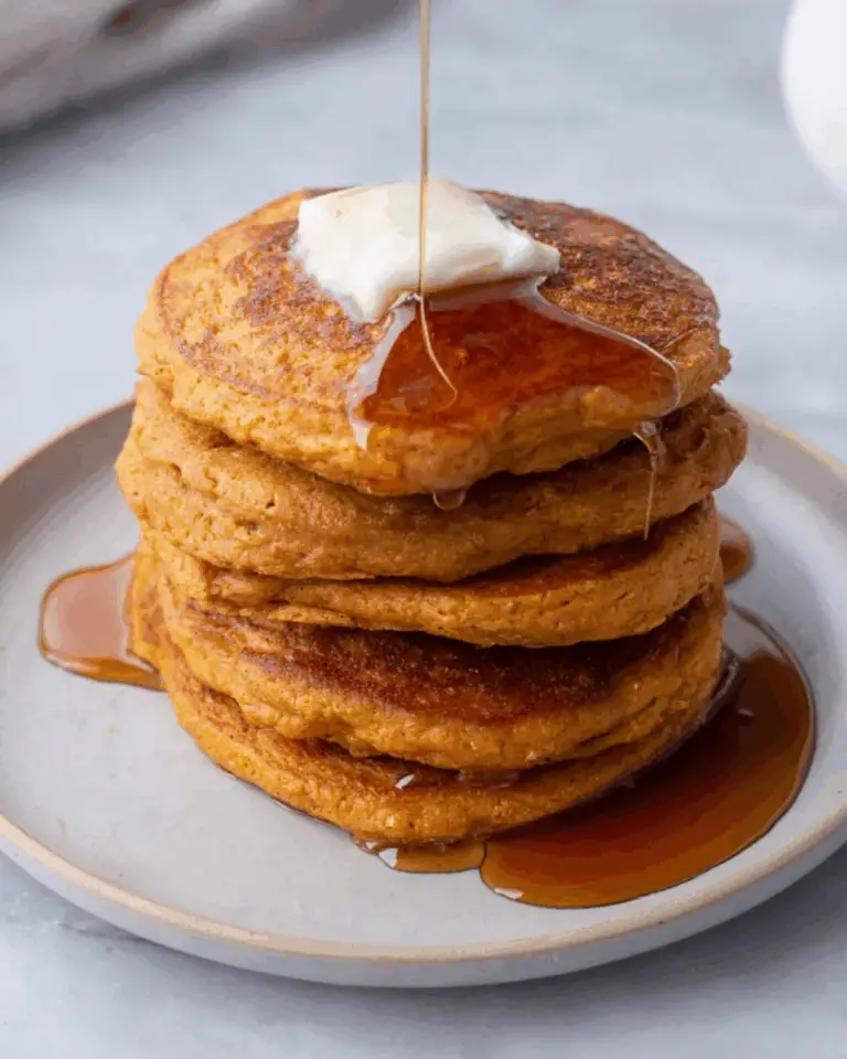 Stack of fluffy sweet potato pancakes topped with butter and drizzled with maple syrup on a white plate.