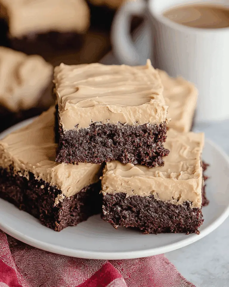 Rich and fudgy Frosted Coffee Brownies with creamy coffee frosting stacked on a white plate beside a cup of coffee.