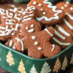 A festive assortment of German gingerbread cookies decorated with white icing in a green holiday-themed tin.
