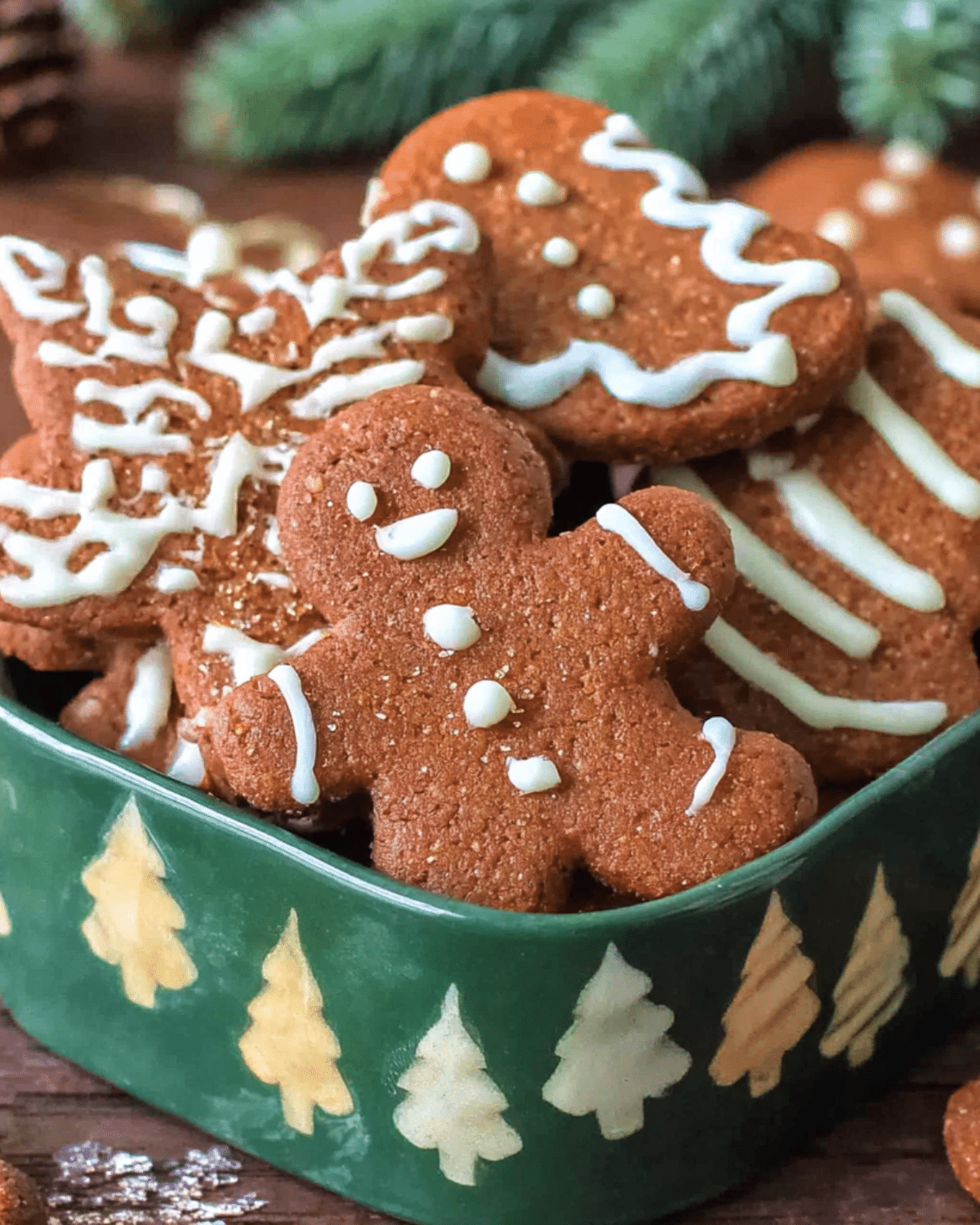 A festive assortment of German gingerbread cookies decorated with white icing in a green holiday-themed tin.