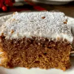 A slice of Gingerbread Crazy Cake topped with powdered sugar and frosting on a white plate.