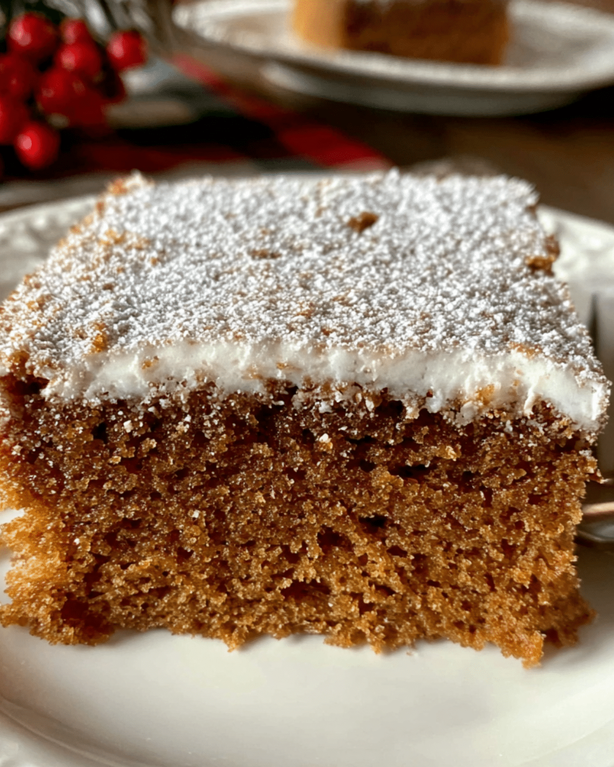 A slice of Gingerbread Crazy Cake topped with powdered sugar and frosting on a white plate.