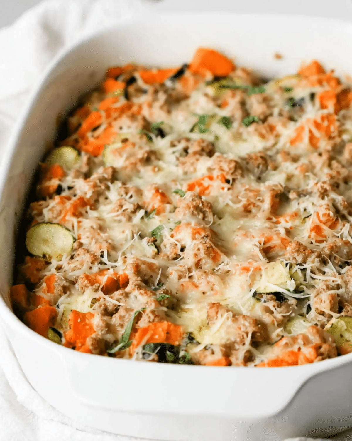 Baked casserole dish filled with Ground Turkey Sweet Potato Bake topped with melted cheese and herbs.