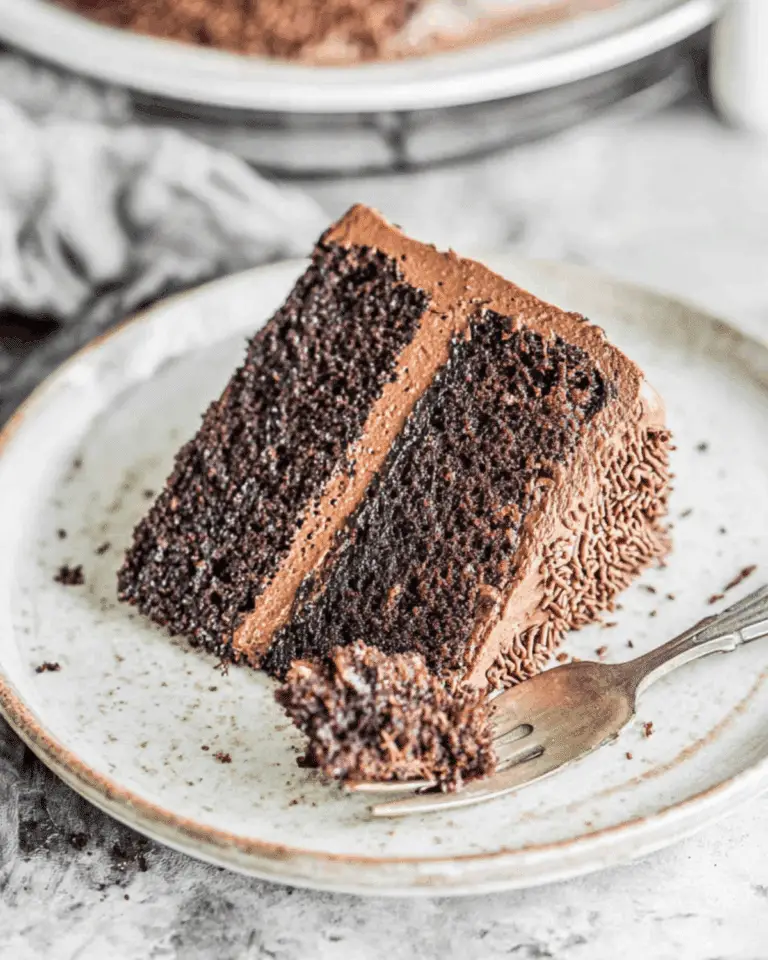 Slice of rich Hershey's Chocolate Cake with chocolate frosting on a plate and a forkful taken.