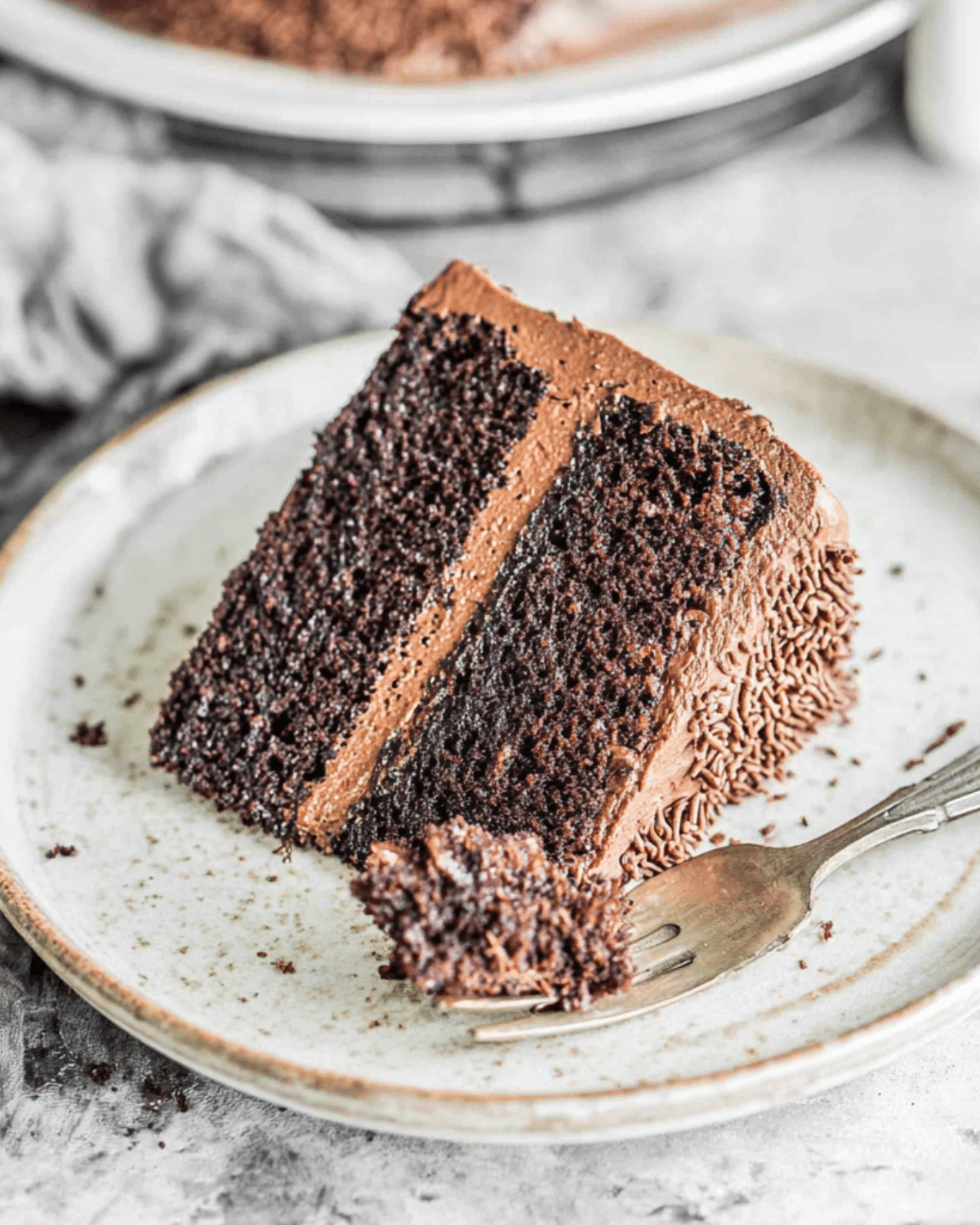 Slice of rich Hershey's Chocolate Cake with chocolate frosting on a plate and a forkful taken.