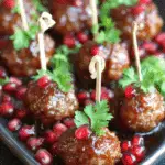 Glazed holiday meatballs garnished with fresh parsley and pomegranate seeds, served on a platter with cocktail picks.