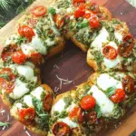 Holiday Wreath Pizza topped with melted mozzarella, cherry tomatoes, pesto, and fresh basil on a wooden board.