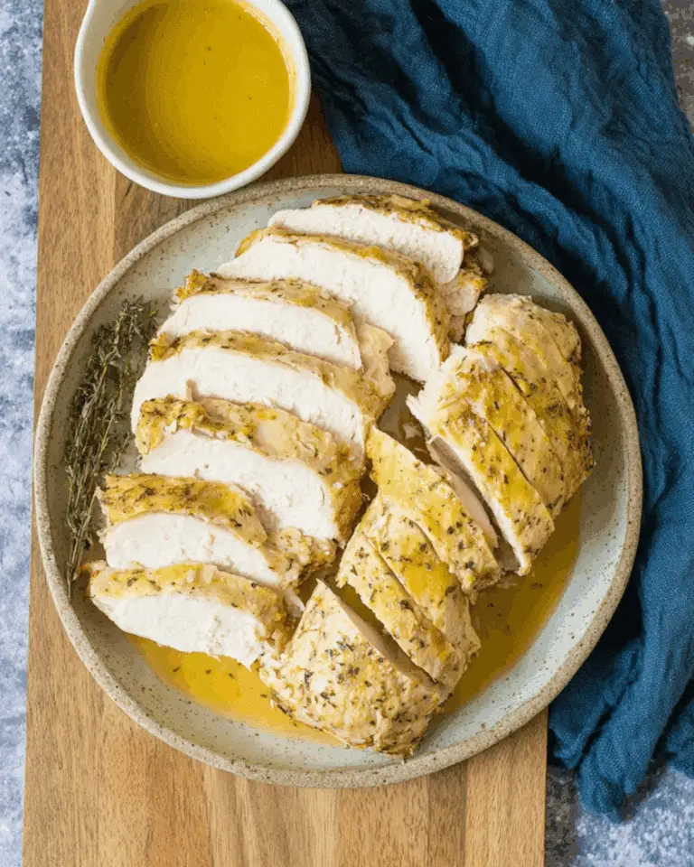 Sliced juicy slow cooker turkey breast served with herb gravy on a ceramic plate with a side of fresh thyme.