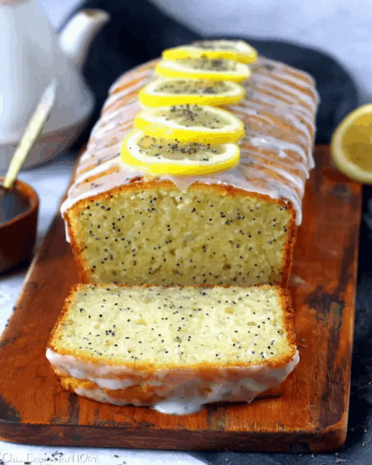 Sliced lemon poppy seed bread topped with icing and lemon slices on a wooden cutting board.