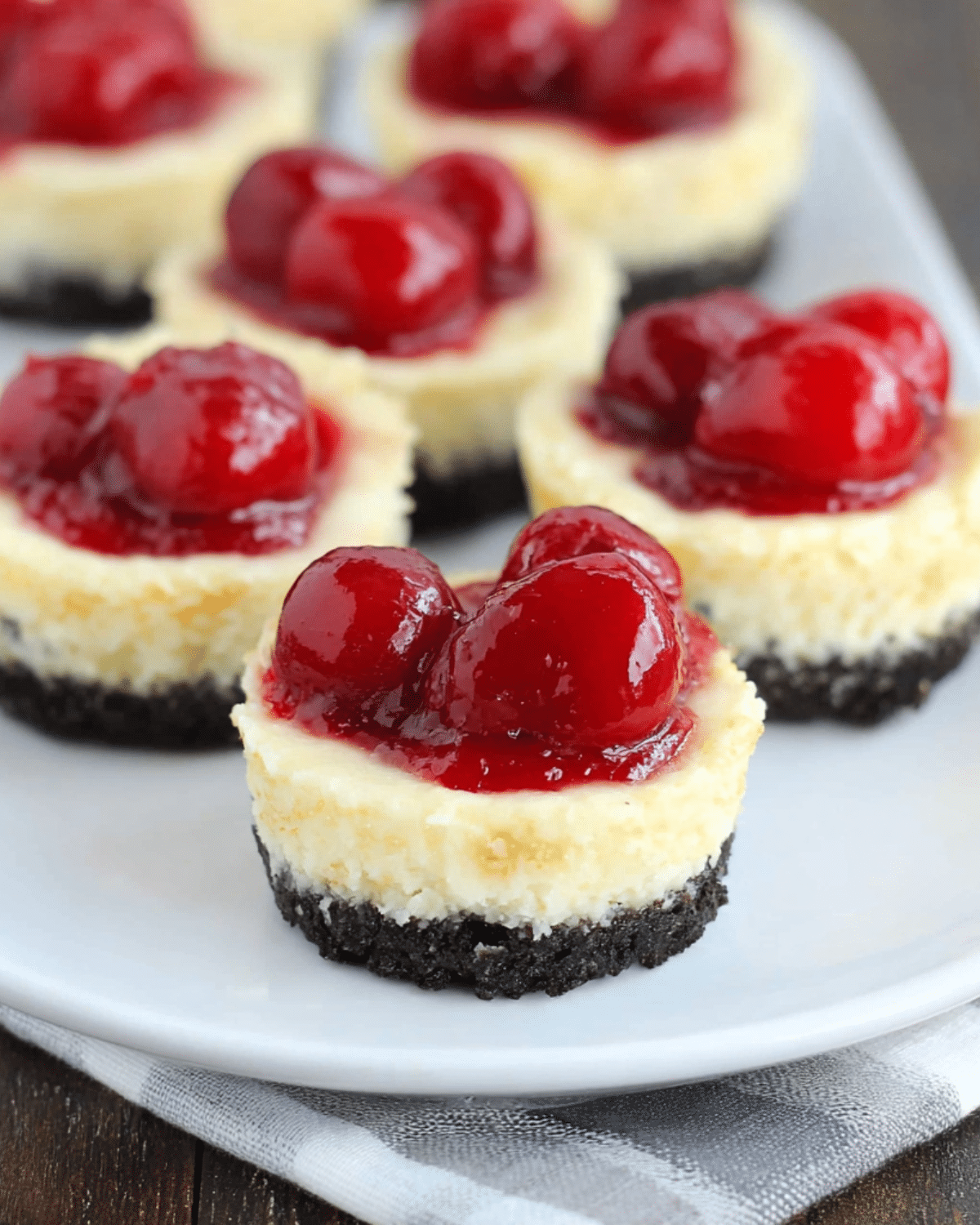 Mini cherry cheesecakes with Oreo crust, topped with glossy cherry pie filling on a white plate.