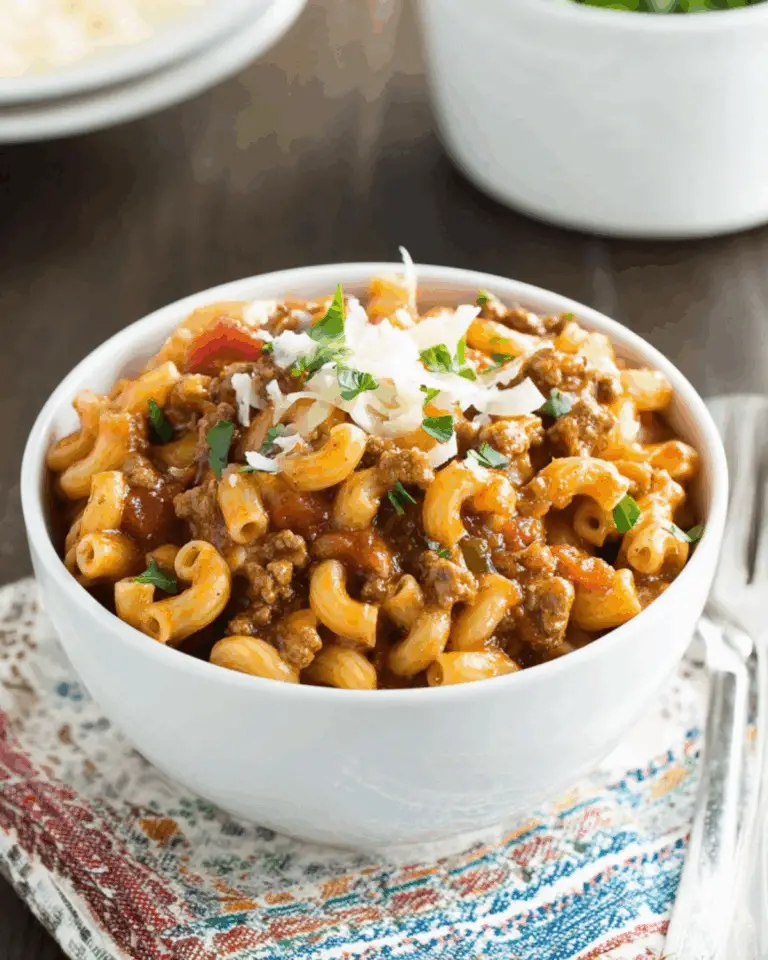 Bowl of one pot mac chili topped with shredded cheese and parsley, served on a colorful napkin.