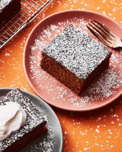 Square slice of Old-Fashioned Gingerbread dusted with powdered sugar on a pink plate.
