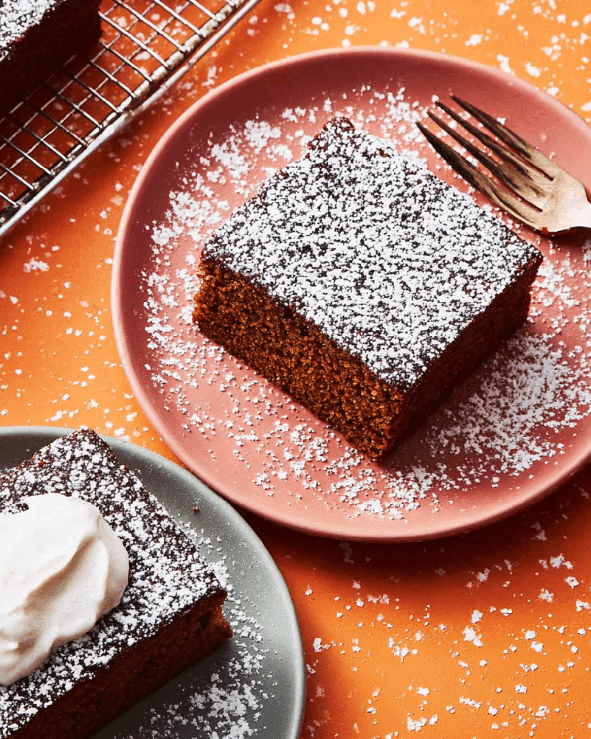 Square slice of Old-Fashioned Gingerbread dusted with powdered sugar on a pink plate.