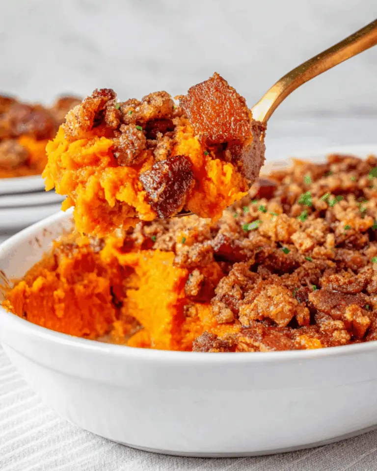 Spoonful of Old-Fashioned Sweet Potato Casserole with a brown sugar and pecan topping held above a white casserole dish.