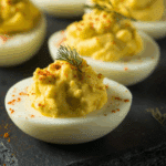 Close-up of Pioneer Woman deviled eggs garnished with dill and paprika on a dark slate platter.