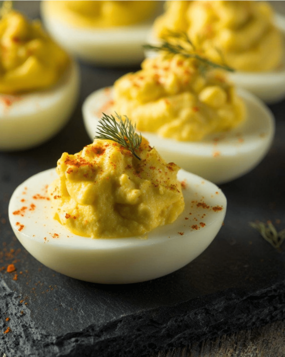 Close-up of Pioneer Woman deviled eggs garnished with dill and paprika on a dark slate platter.