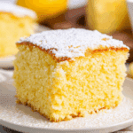 A slice of fluffy Portuguese orange cake topped with powdered sugar on a white plate.