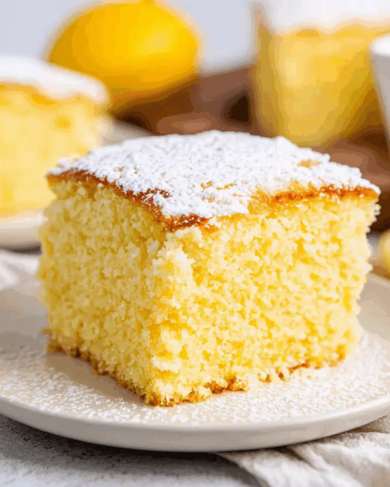 A slice of fluffy Portuguese orange cake topped with powdered sugar on a white plate.