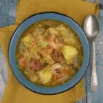 A bowl of Potato, Leek & Chorizo Soup with chunks of potatoes, sliced chorizo, shrimp, and leeks in a flavorful broth.
