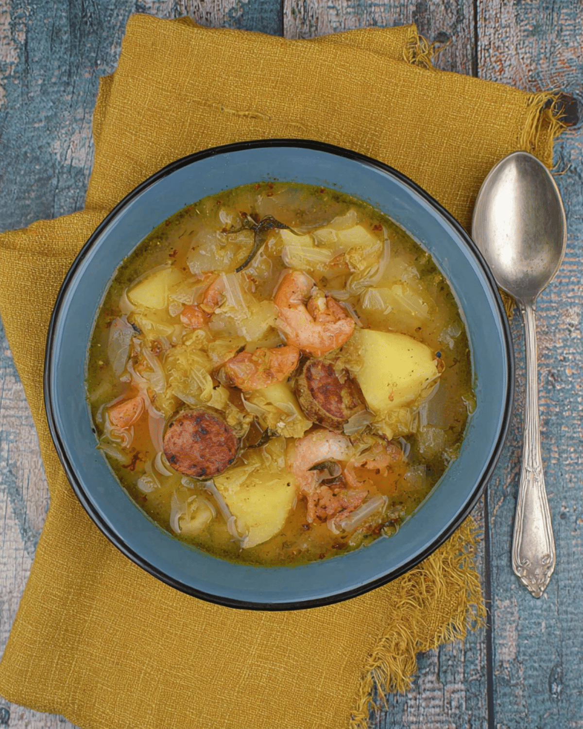A bowl of Potato, Leek & Chorizo Soup with chunks of potatoes, sliced chorizo, shrimp, and leeks in a flavorful broth.