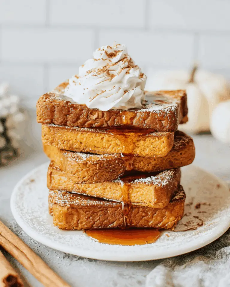 A stack of pumpkin French toast slices topped with whipped cream, powdered sugar, and drizzled with maple syrup.