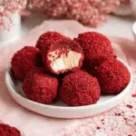 Plate of red velvet cheesecake bites with one bite showing creamy cheesecake filling inside.