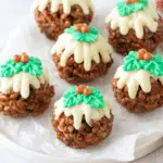 Festive Rice Krispie Christmas puddings topped with white chocolate, green icing holly leaves, and red candy berries.