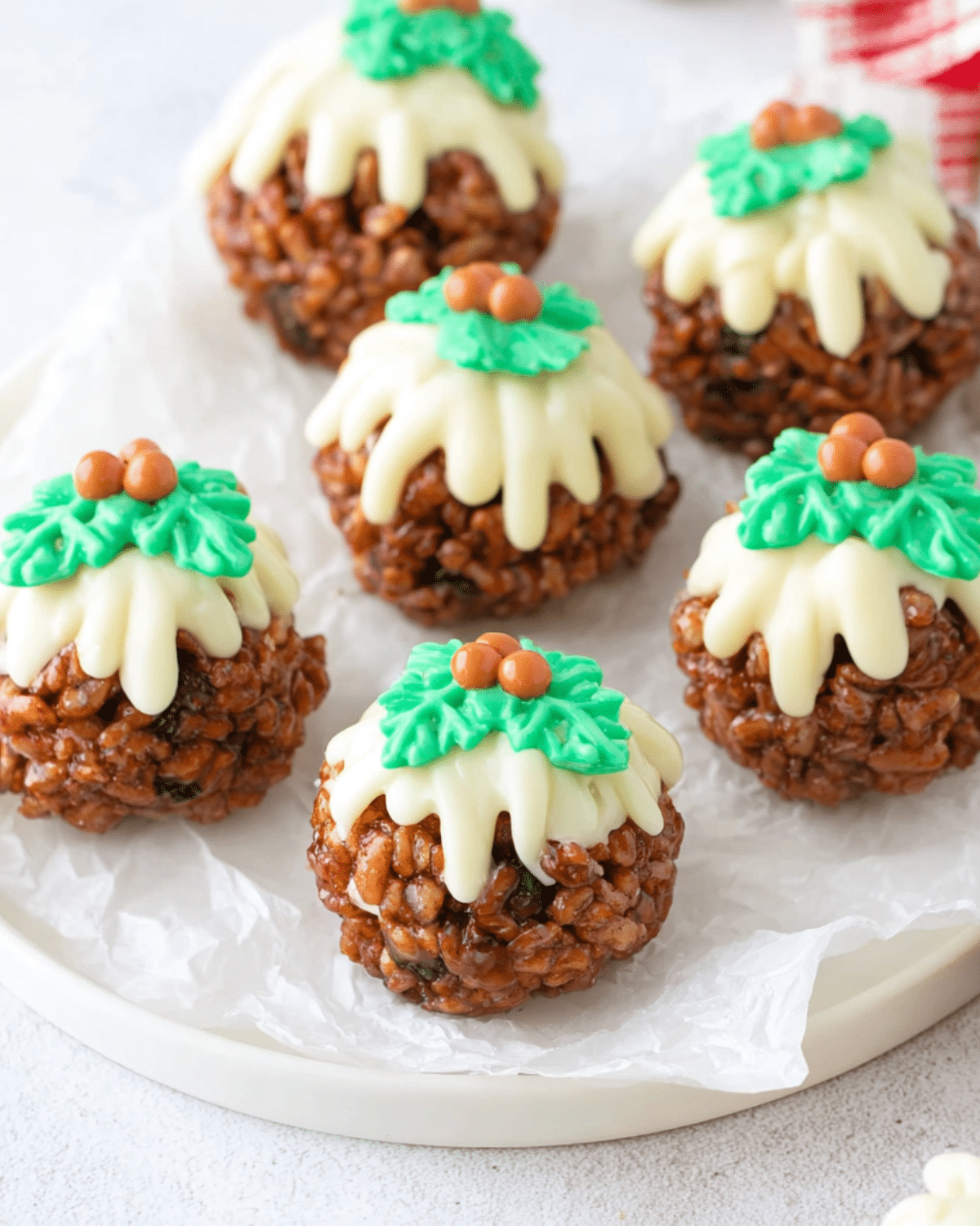Festive Rice Krispie Christmas puddings topped with white chocolate, green icing holly leaves, and red candy berries.