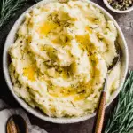 Bowl of rosemary garlic mashed potatoes topped with melted butter and fresh herbs.