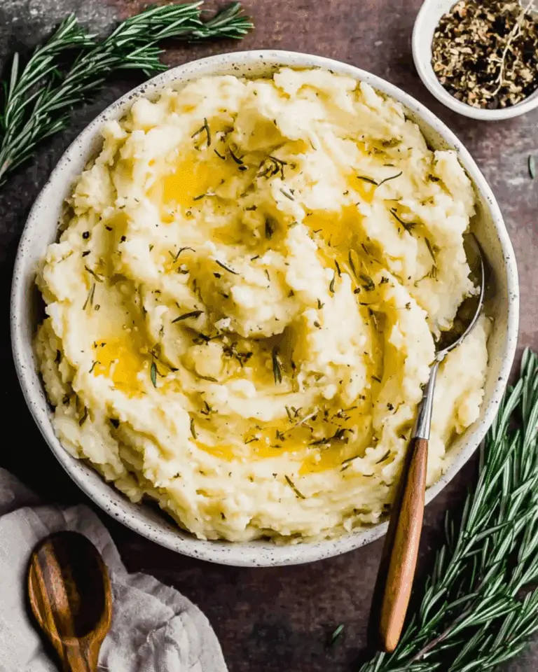 Bowl of rosemary garlic mashed potatoes topped with melted butter and fresh herbs.