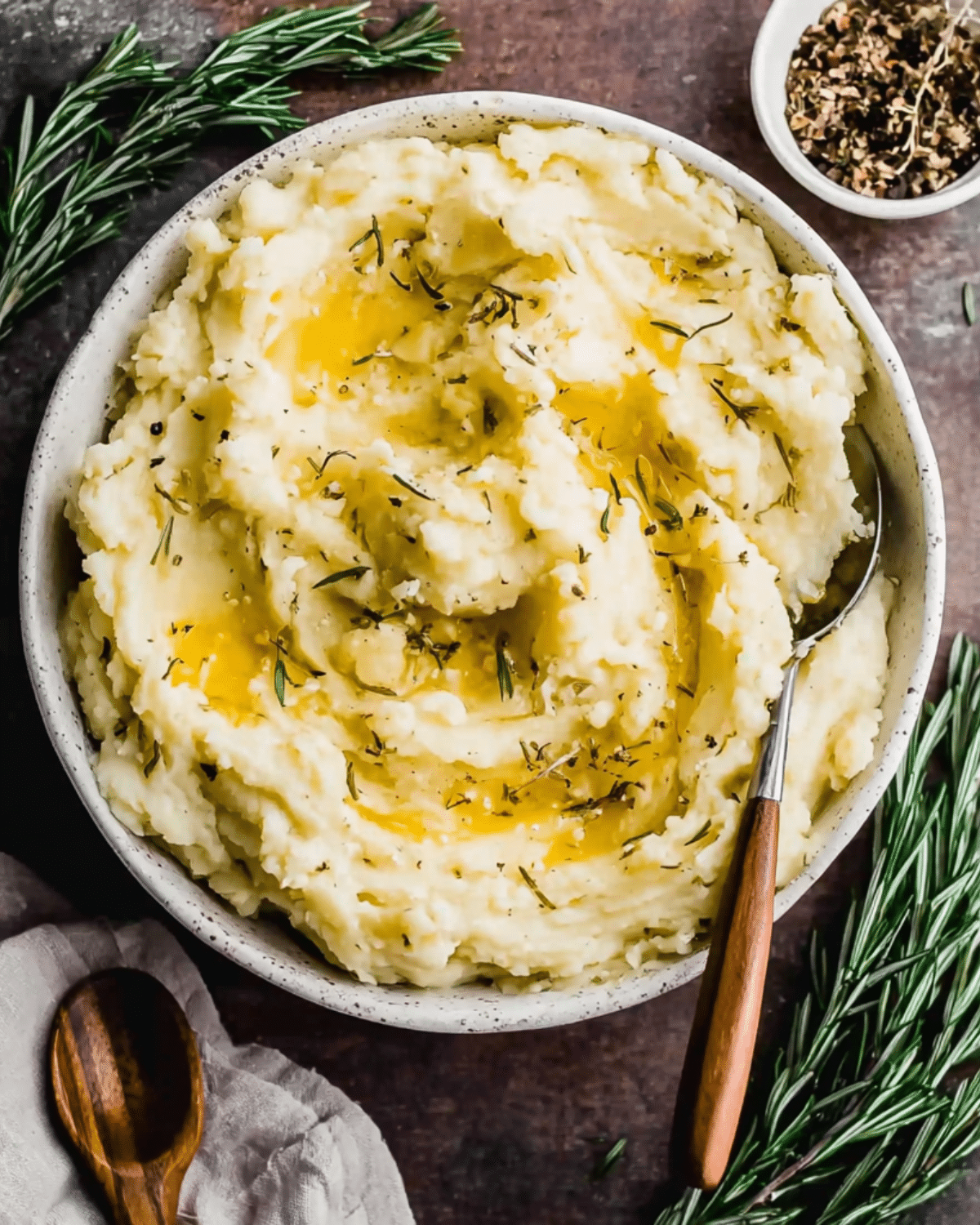 Bowl of rosemary garlic mashed potatoes topped with melted butter and fresh herbs.