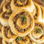 Golden sausage pinwheels made with biscuit dough, filled with savory sausage and topped with herbs.