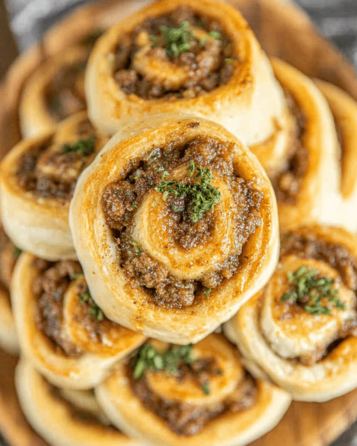 Golden sausage pinwheels made with biscuit dough, filled with savory sausage and topped with herbs.