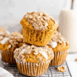 Sweet Potato Muffins topped with crumbly streusel and icing, stacked on a cooling rack.