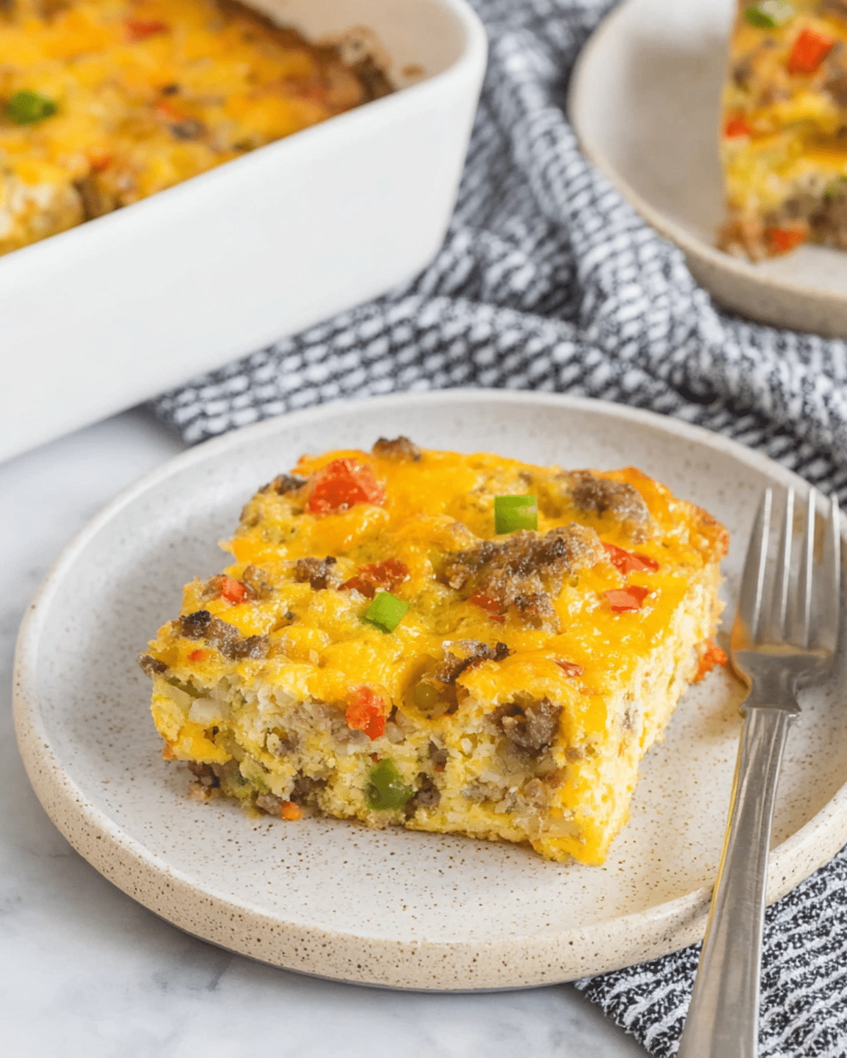 A slice of Tater Tot Breakfast Casserole with sausage, cheese, and vegetables served on a ceramic plate.