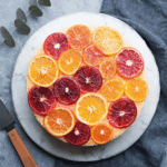 A beautifully arranged Upside-Down Ombré Citrus Cake topped with vibrant slices of blood oranges, oranges, and mandarins on a marble plate.