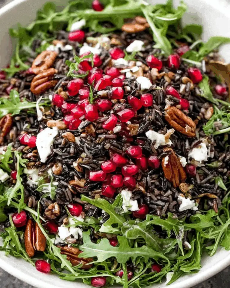 Wild rice salad with arugula, pecans, goat cheese, and pomegranate seeds in a white bowl.